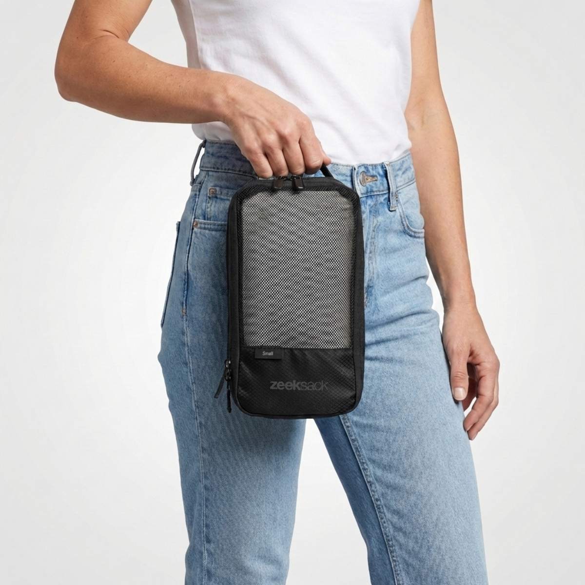 Kvinne i hvit t-skjorte og jeans holder en svart pakkekube med nettlomme på forsiden.