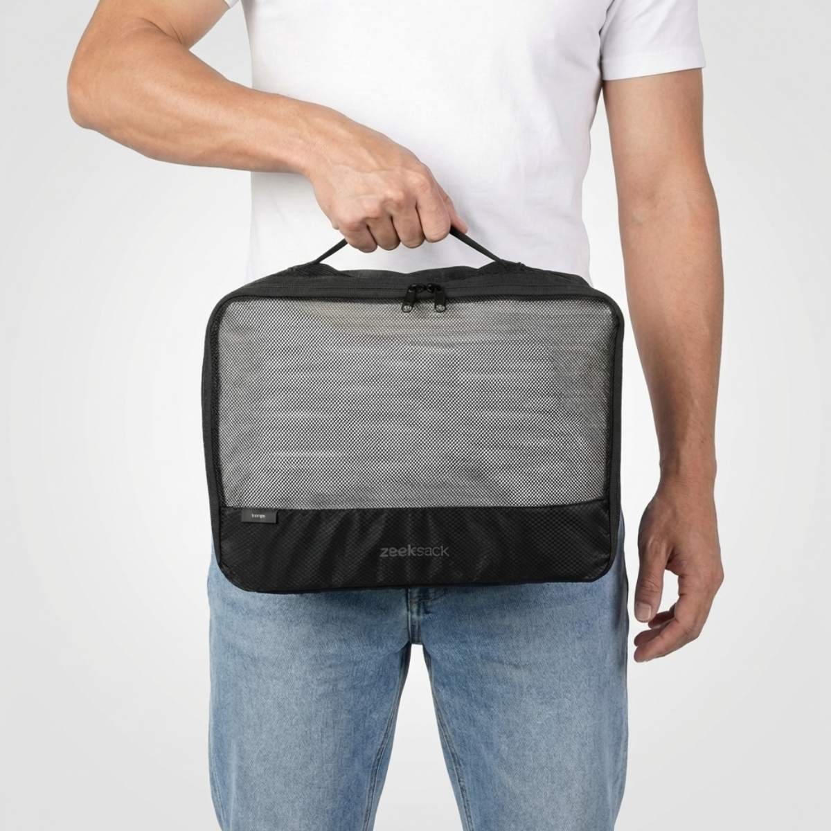 Mann i hvit t-skjorte og jeans holder en stor svart pakkekube med nettlomme på forsiden.