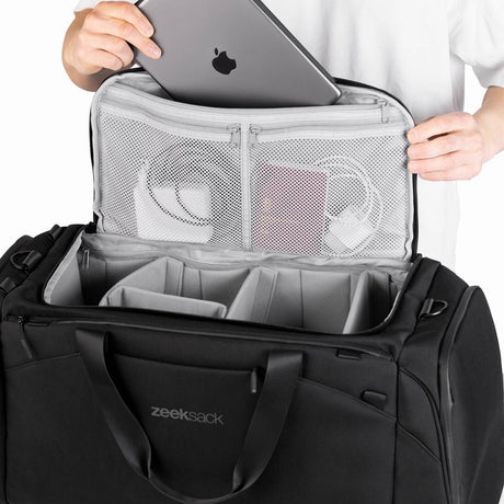 The Duffelbag med lokket åpent, viser mesh-lommer med pass og kabler, samt laptop som tas ut.