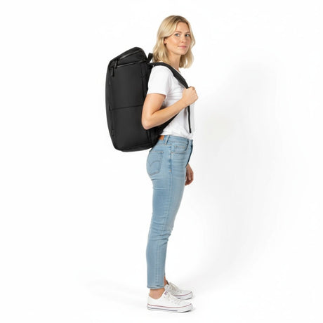 Kvinne i hvit t-skjorte og jeans bærer en svart Zeeksack-ryggsekk, sett fra siden.