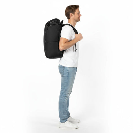 Mann i hvit t-skjorte og jeans bærer en svart Zeeksack-ryggsekk, sett fra siden.
