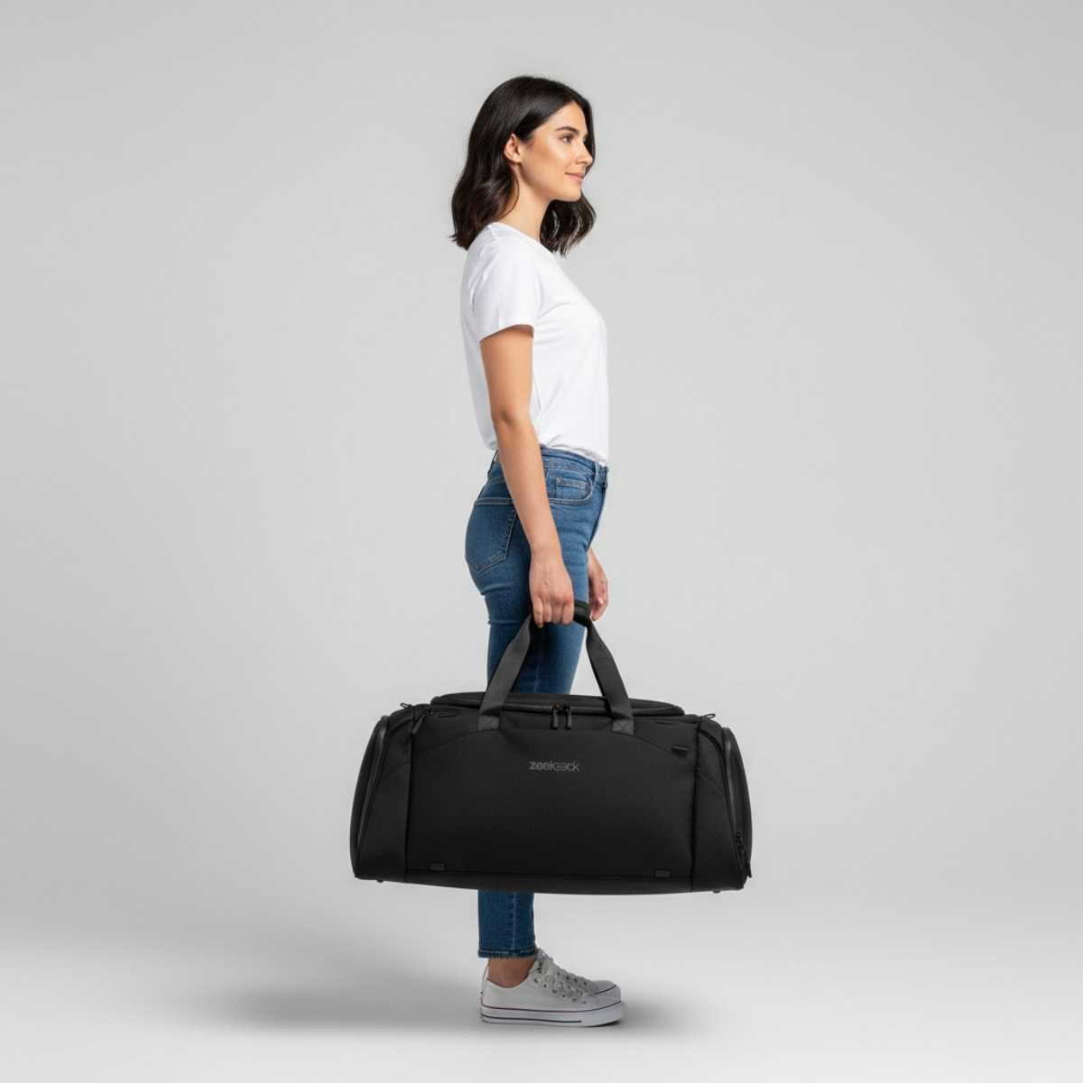 Kvinne i hvit t-skjorte og jeans holder en svart duffelbag i hånden.