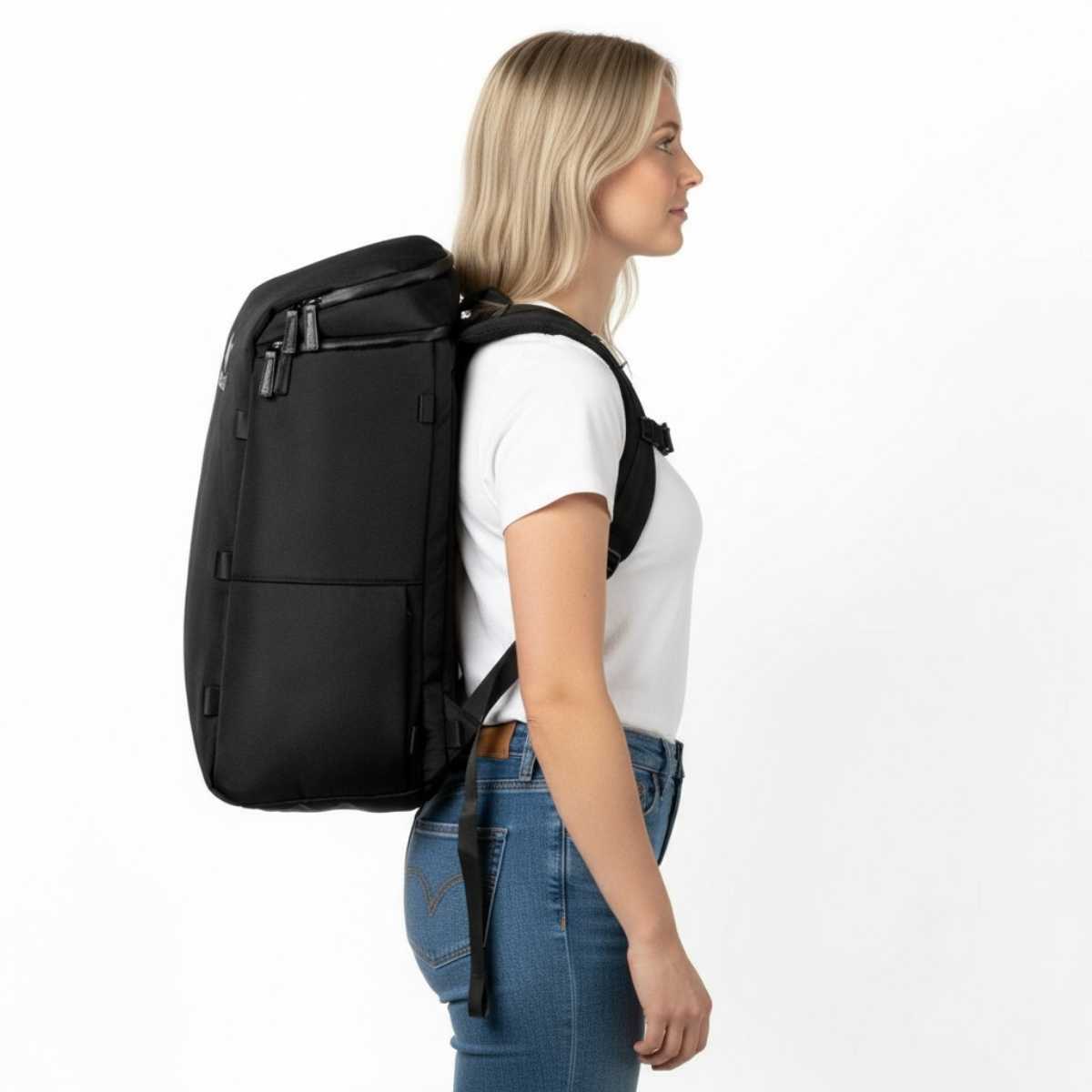 Kvinne i hvit t-skjorte og jeans står i profil med en svart ryggsekk på ryggen.