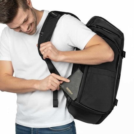Mann i hvit t-skjorte og jeans strammer en stropp på en svart ryggsekk.