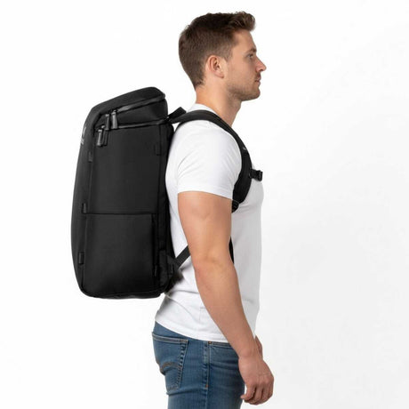 Mann i hvit t-skjorte og jeans står i profil med en svart ryggsekk på ryggen.