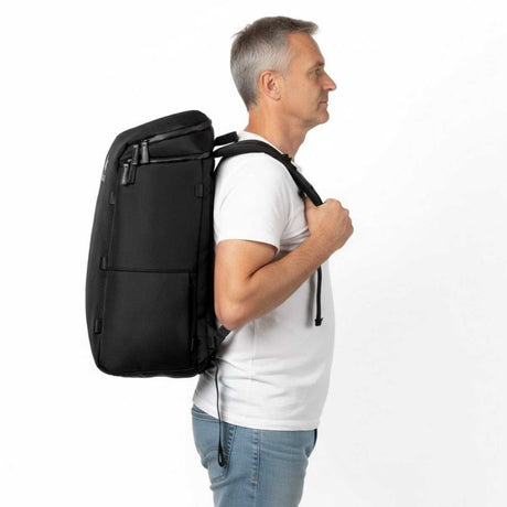 Mann i hvit t-skjorte og jeans står i profil mot venstre med en svart ryggsekk på ryggen.