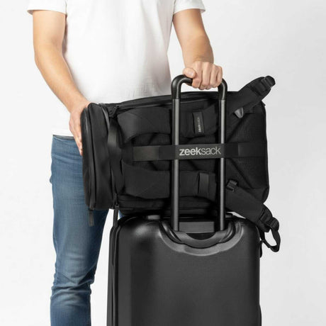 Mann i hvit t-skjorte og jeans setter en svart ryggsekk på håndtaket til en koffert.