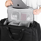 The Duffelbag med lokket åpent, viser mesh-lommer med pass og kabler, samt laptop som tas ut.