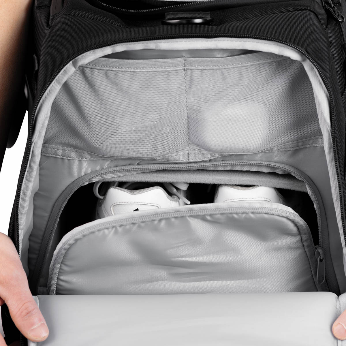 Nærbilde av The Duffelbags åpne skofack med hvite sneakers og lomme for småting.
