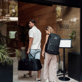 Zeeksack - Kvinne med The Organizer 30L på ryggen og mann med The Weekender 50L i hånden på vei inn på et hotell.