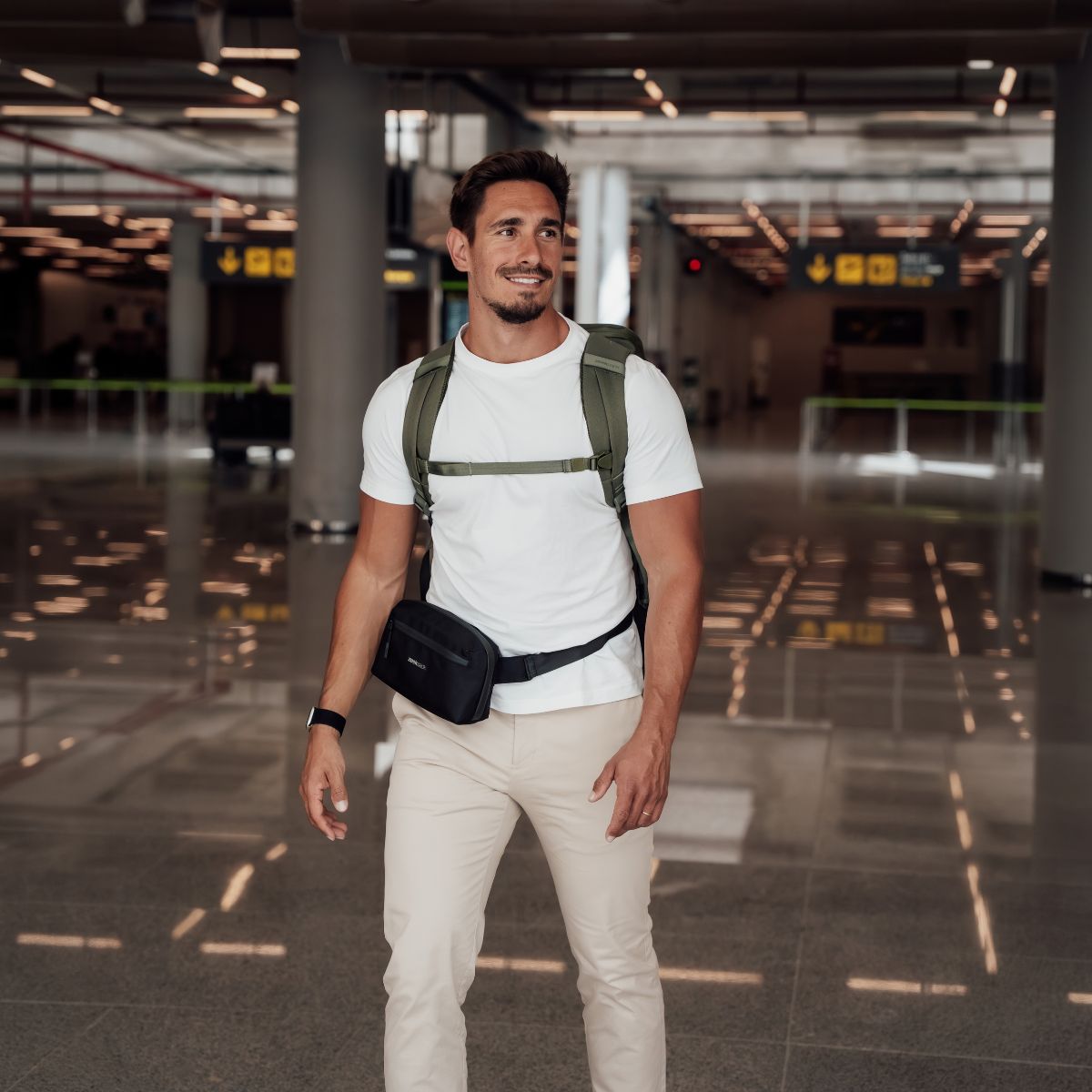 Zeeksack - Mann med The Underseat 15L på ryggen og Crossbody Organizer rundt livet på en flyplass.